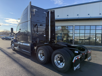 New Mack PR64T76H tractor in service bay showing cab side and rear wheels; visible text includes Mack branding on mudflaps and stock number placard near rear; large cab with aerodynamic design.
