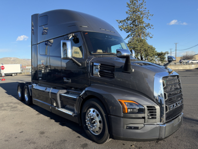 Mack PR64T76H tractor-trailer truck front-left view showing glossy black sleeper cab, chrome grille, mirrors, and dual rear axles.
