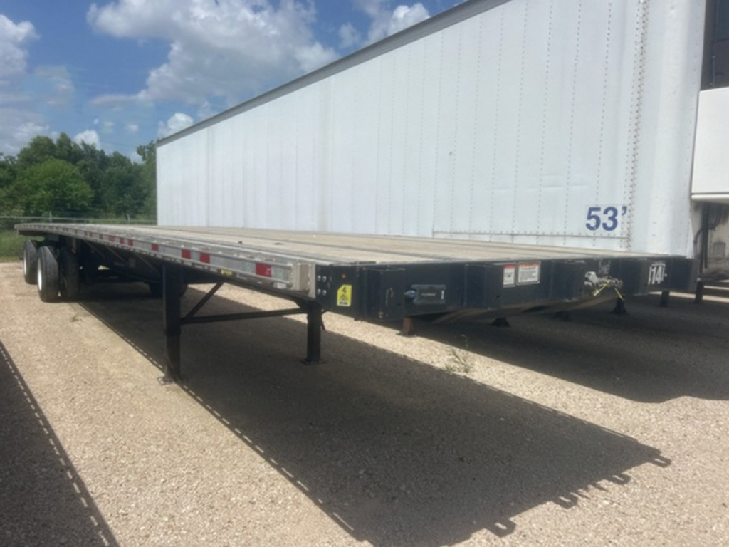 Great Dane Freedom LT flatbed trailer showing 53' length with dual axles and gooseneck design, parked near a white warehouse.