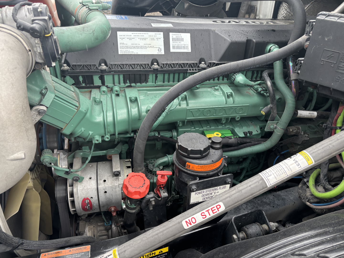 Volvo VNL84T300 under-hood view showing green Volvo engine, belts, radiator, coolant reservoir, and various hoses with labels like NO STEP.