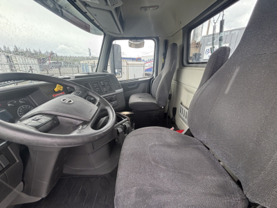 Truck cab interior showing steering wheel and dashboard of a Volvo VNL84T300 with grey fabric seats.