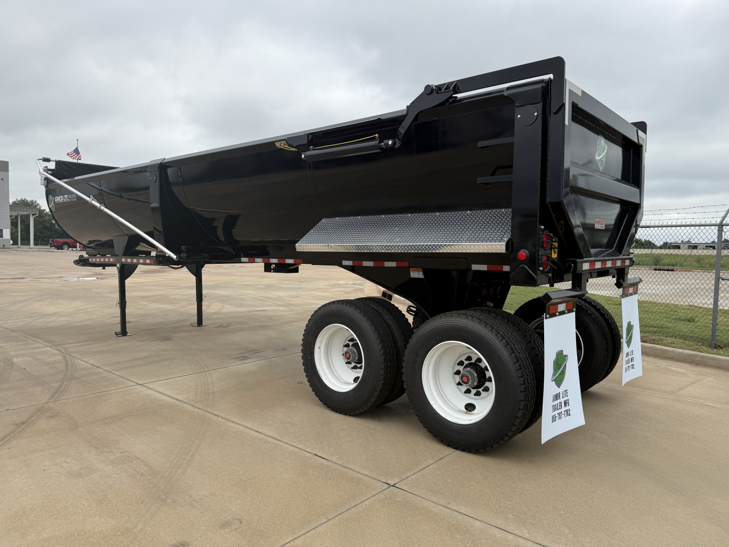 Armor Lite SHD32/48 dump trailer showing dual axles with white rims, black bed, and reflective tape. VIN 56EA75C22VA000204 on listing, stickered information visible.
