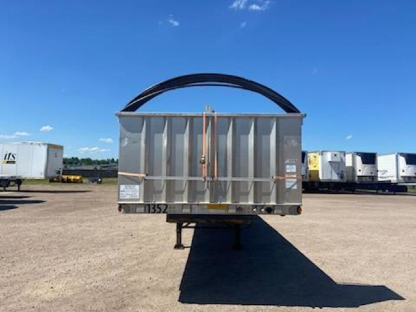 Rear view of a flatbed trailer with a curved metal gooseneck hook above the bed; side and rear panels visible with some labeling.