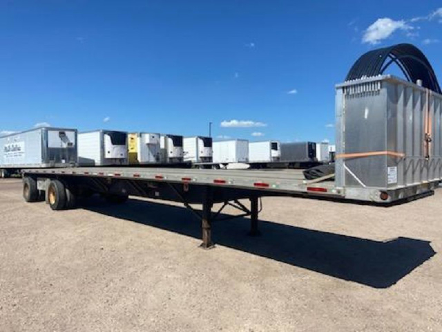 Flatbed trailer with multiple refrigerated units and a coiled hose reel at the front right; long metal deck with support legs extended.