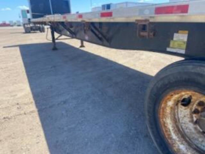 Flatbed trailer side view showing undercarriage and wheel with rusted rim.