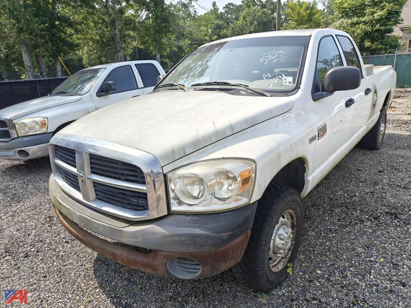 Dodge Ram 2500 crew cab pickup truck in on-site lot, white with black side mirrors, front bumper and grille. Visible badges and 4x4, worn body with dirt.