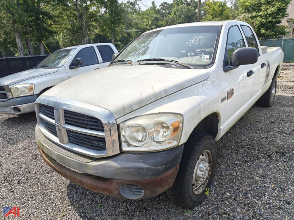 Dodge Ram 2500 crew cab pickup truck in on-site lot, white with black side mirrors, front bumper and grille. Visible badges and 4x4, worn body with dirt.