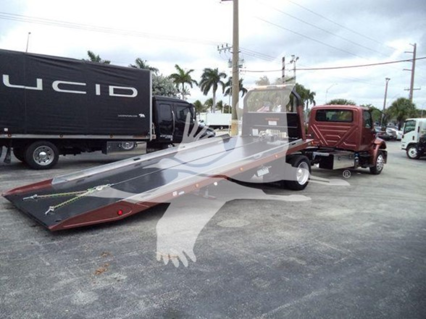 Roll-back truck with flatbed trailer and a red tow vehicle in background; image shows a large glossy black and gray ramp and a Lucid truck trailer in a dealership lot.
