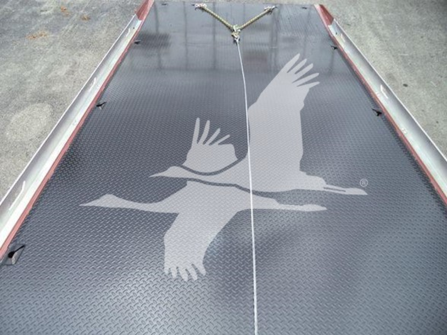 Truck bed or loading area with a textured black surface featuring a white silhouette of two birds in flight and a central white line.