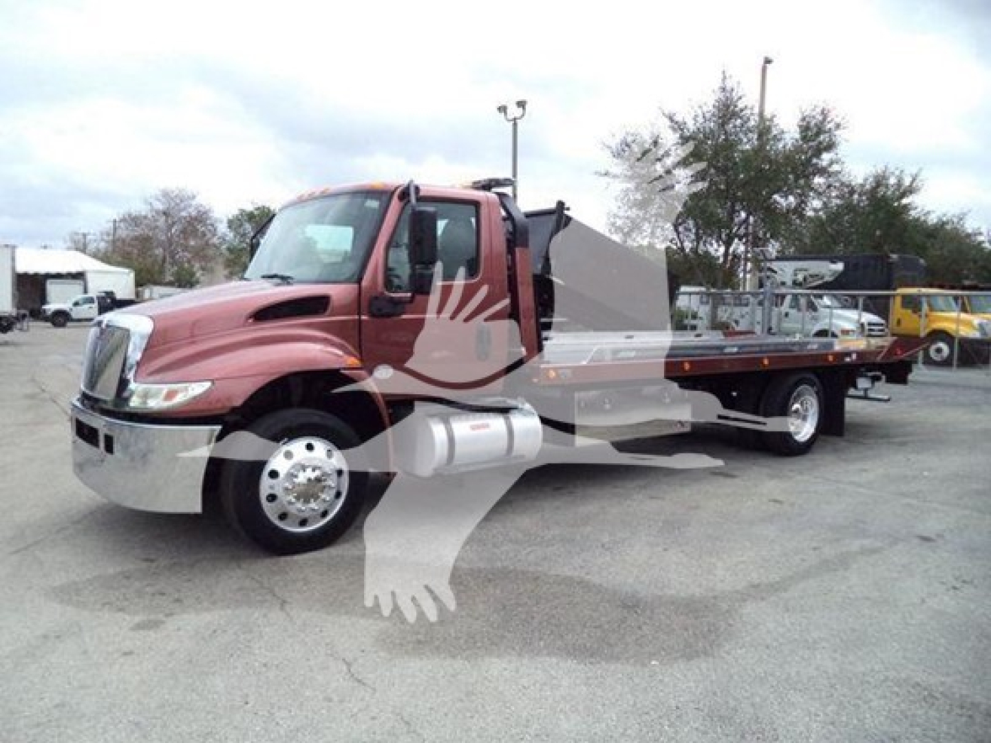 Truck with a flatbed/rollback body showing red cab and long flatbed; a faded watermark graphic overlay is present.