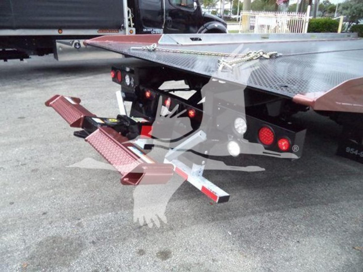 Truck equipment showing a hydraulic rollback bed with side steps and rear bumper, platform and safety chains visible.