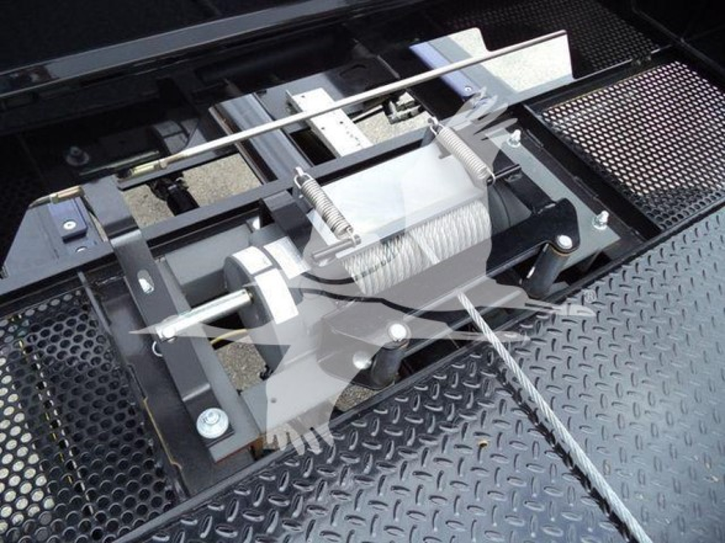 Winch mechanism and metal deck of a rollback truck with a visible winch reel and steel cable, crossbar, and mounting brackets.