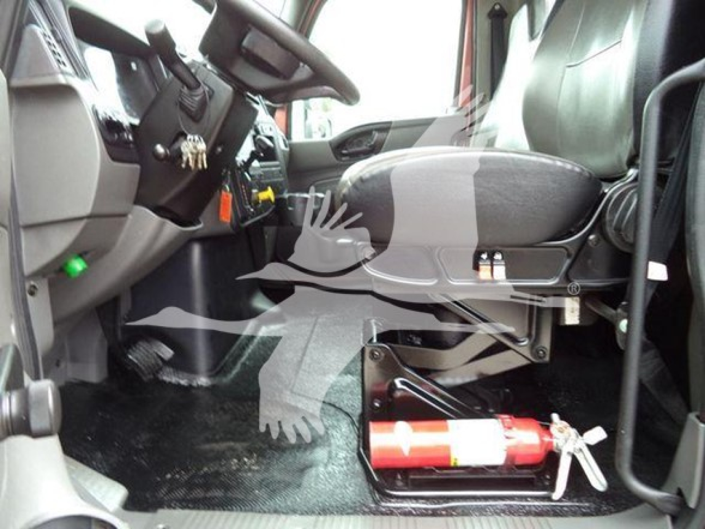 Truck cab interior of a 2020 International MV with a fire extinguisher mounted under the dashboard near the driver seat and pedals visible.