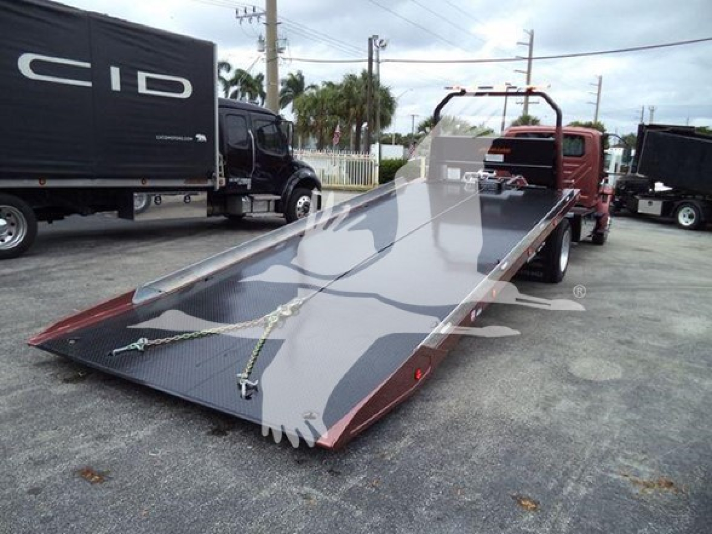Flatbed tow truck platform with chain tie-downs and ramp, International MV rollback truck in a used inventory yard.
