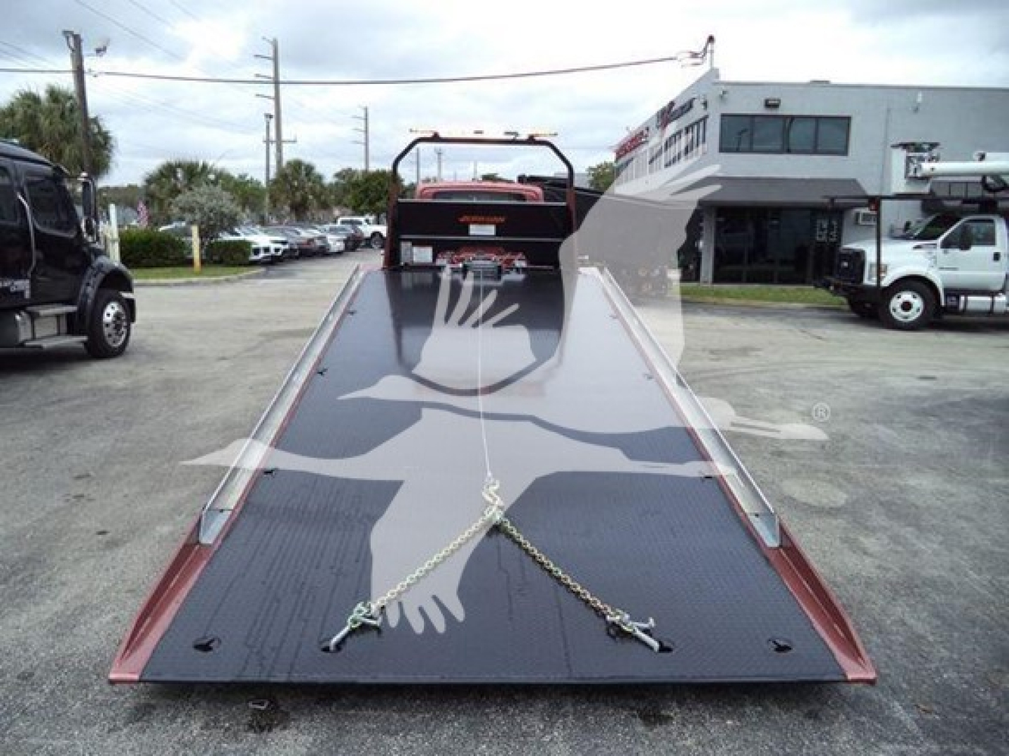 Tow truck rollback bed with chains and winch in foreground, view down the ramp toward cab, International MV model information not visible.