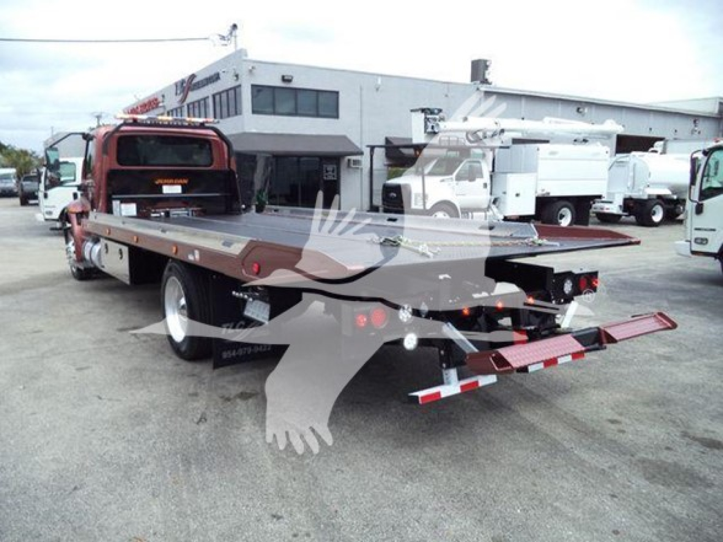 Tow truck rollback flatbed of a 2020 International MV with extended bed and rear hydraulic ramps, viewed from rear-left side in a dealership lot.
