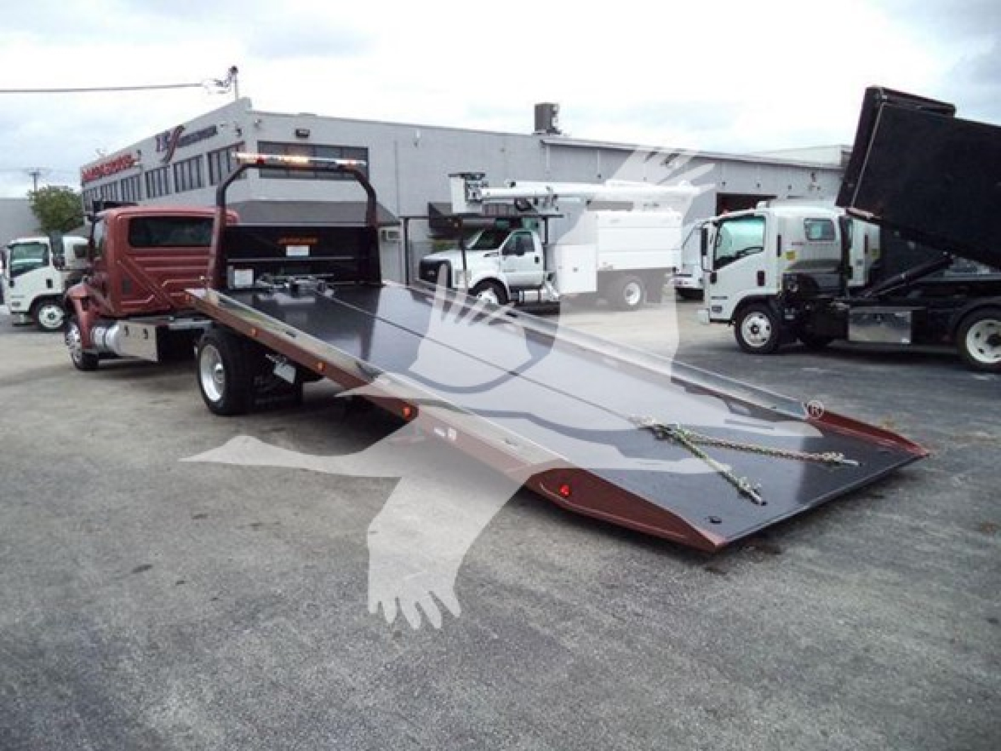 Tow truck with a lowered flatbed in a dealership lot showing a heavy-duty rollback truck.