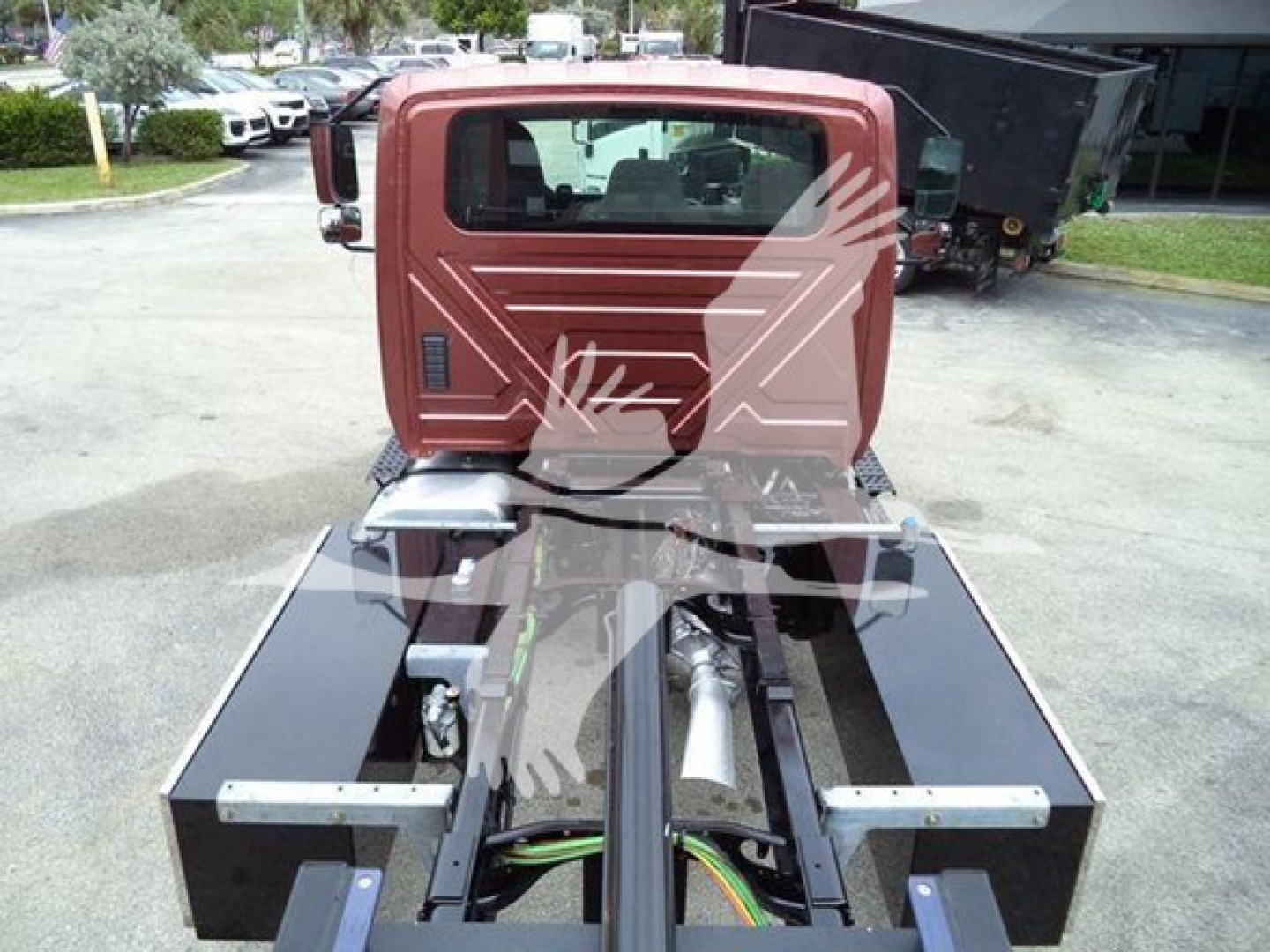 Truck cab rear view showing chassis and hydraulic components in a rollback truck. Visible components include a black frame, green and yellow wires, and a red cab with rear window.