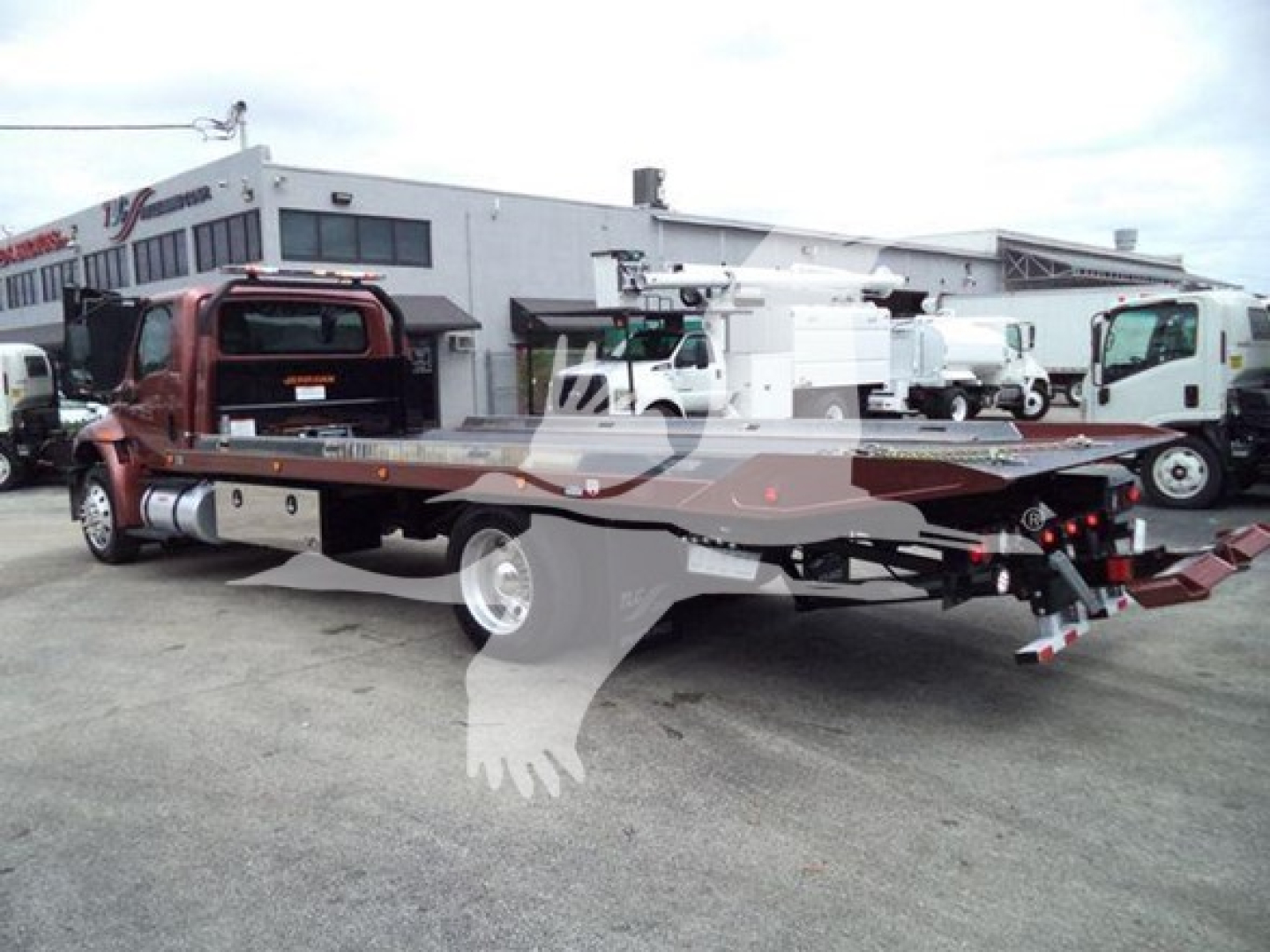 2020 International MV rollback truck with long flatbed trailer in a lot, side view showing cab and chassis