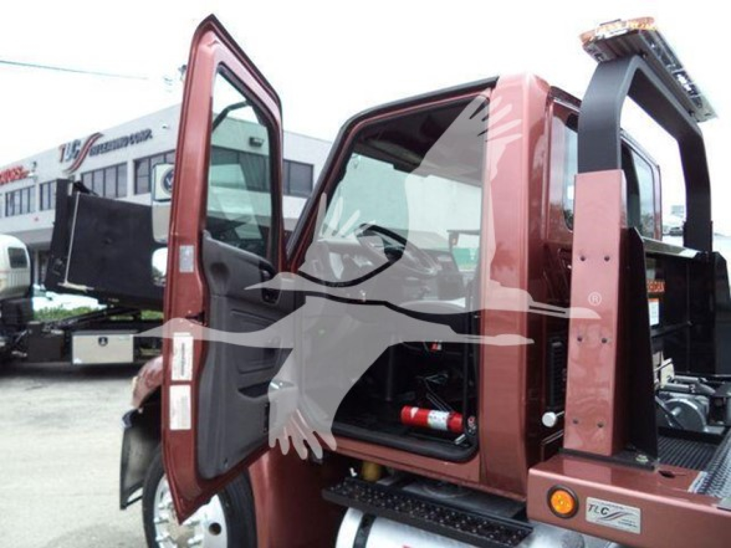 Truck cab interior with doors open; rear hydraulic rollback equipment visible; side door jamb labels and a fire extinguisher inside.