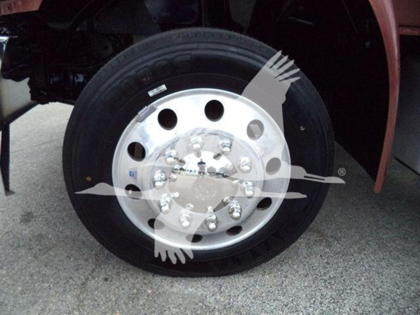 Truck wheel and tire showing polished aluminum hub with lug nuts and circular holes, front fender area visible.