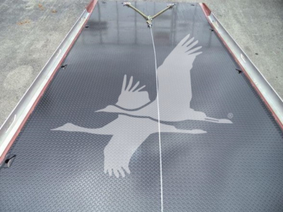 Truck bed or loading area with a textured black surface featuring a white silhouette of two birds in flight and a central white line.