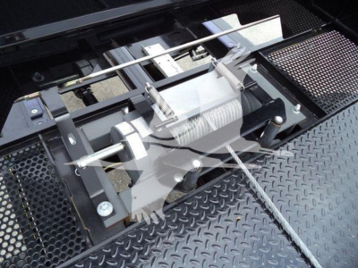 Winch mechanism and metal deck of a rollback truck with a visible winch reel and steel cable, crossbar, and mounting brackets.