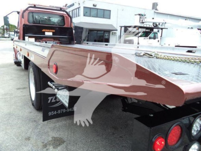 Tow truck flatbed rollback showing side of flatbed with metal diamond plate; rear wheels and taillights visible; VIN and stock label not legible.