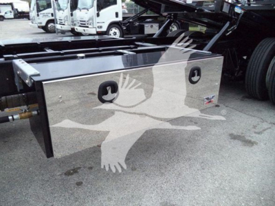 Truck bed toolbox mounted under the chassis of a 2020 International MV rollback vehicle showing a polished rectangular aluminum toolbox with two cutouts and mounting hardware.