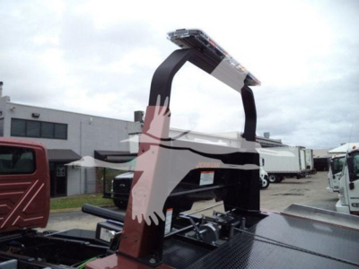 Truck bed with a heavy-duty rollback hoist arching over; no legible brand text visible; surroundings show a vehicle lot with other trucks.