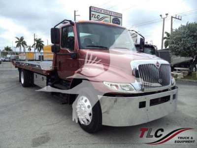 International MV rollback truck showing front grille, chrome bumper, dual rear crew cab mirror, and flatbed with side steps.