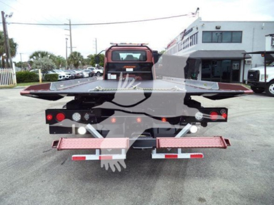 Trucking flatbed tow truck rear view with hydraulic ramps and taillights, working area, and stock yard background.