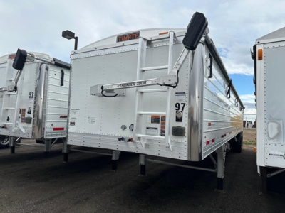 Timpte Super Hopper trailer in a lot, side view shows Thunder 7000 hydraulic tailgate and landing legs. Brand plate 'Timpte' visible on top front, number 97 on side.