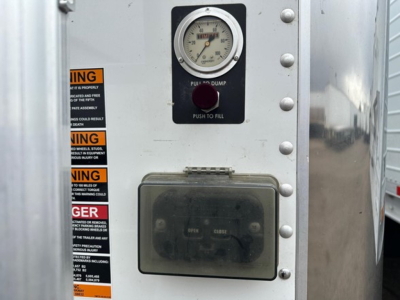 Trailer control panel of a 2024 Timpte Super Hopper showing a gauge, push to fill button, and a metal access panel with labels and rivets.
