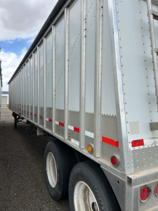 Grain hopper trailer side view showing metal panels, riveted construction, and dual rear wheels.
