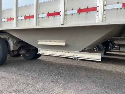 Hopper trailer underside showing grain hopper with unloading chute and axles. Side rail and reflective tape visible.