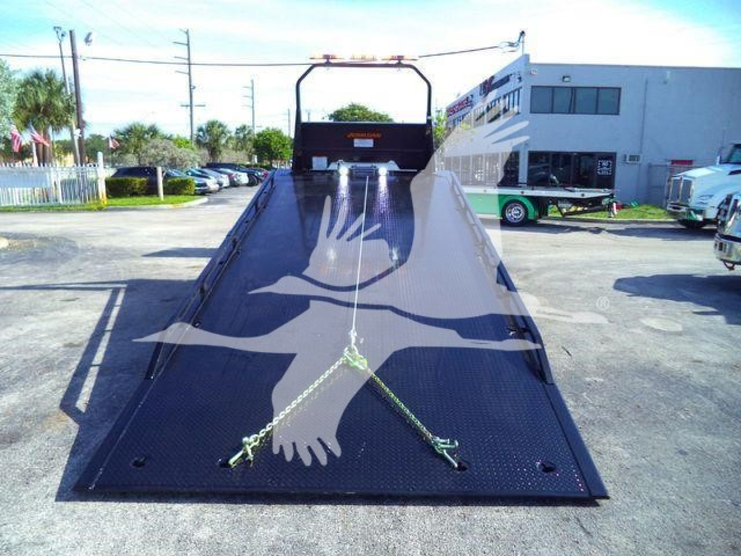 Truck bed of a 2026 Peterbilt 536 rollback showing a long metal loading ramp with a front winch and safety chains.