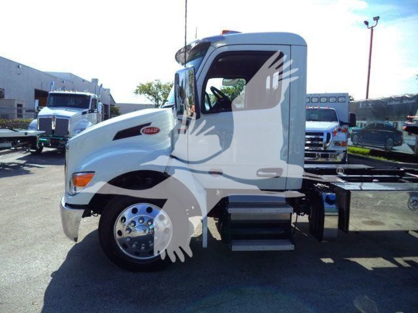 Peterbilt truck cab side view showing front wheel, door and cab with Rollback chassis in a dealership lot.