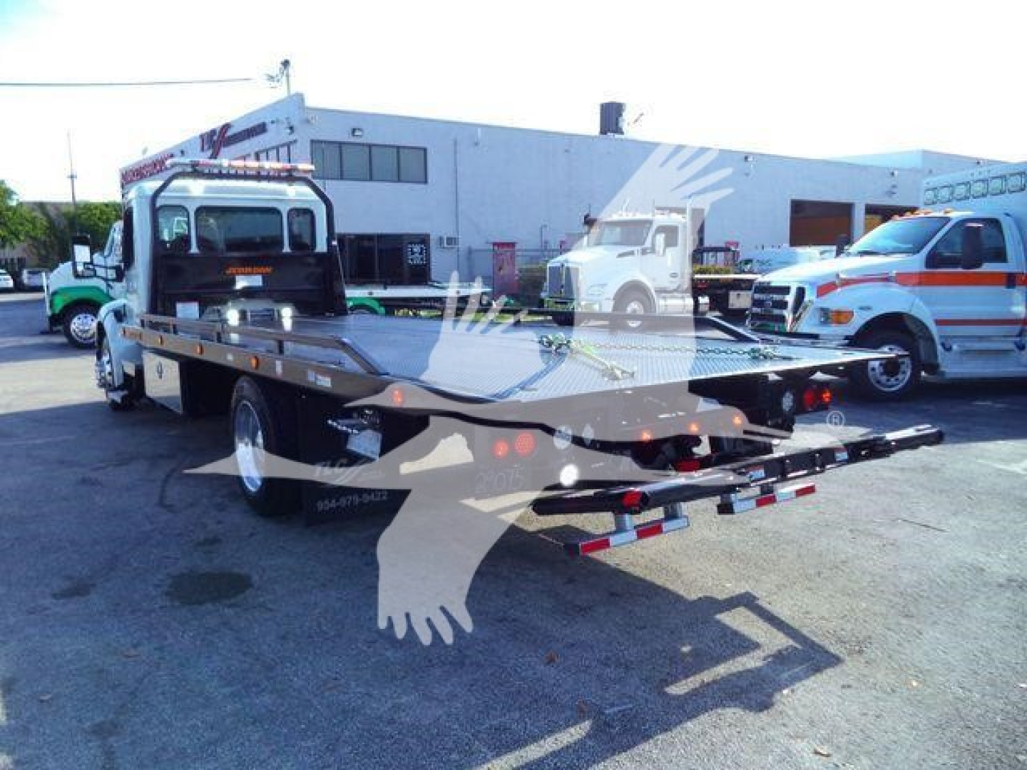 Flatbed tow truck with rollback in lot showing Peterbilt 536 cab and flatbed bed area.