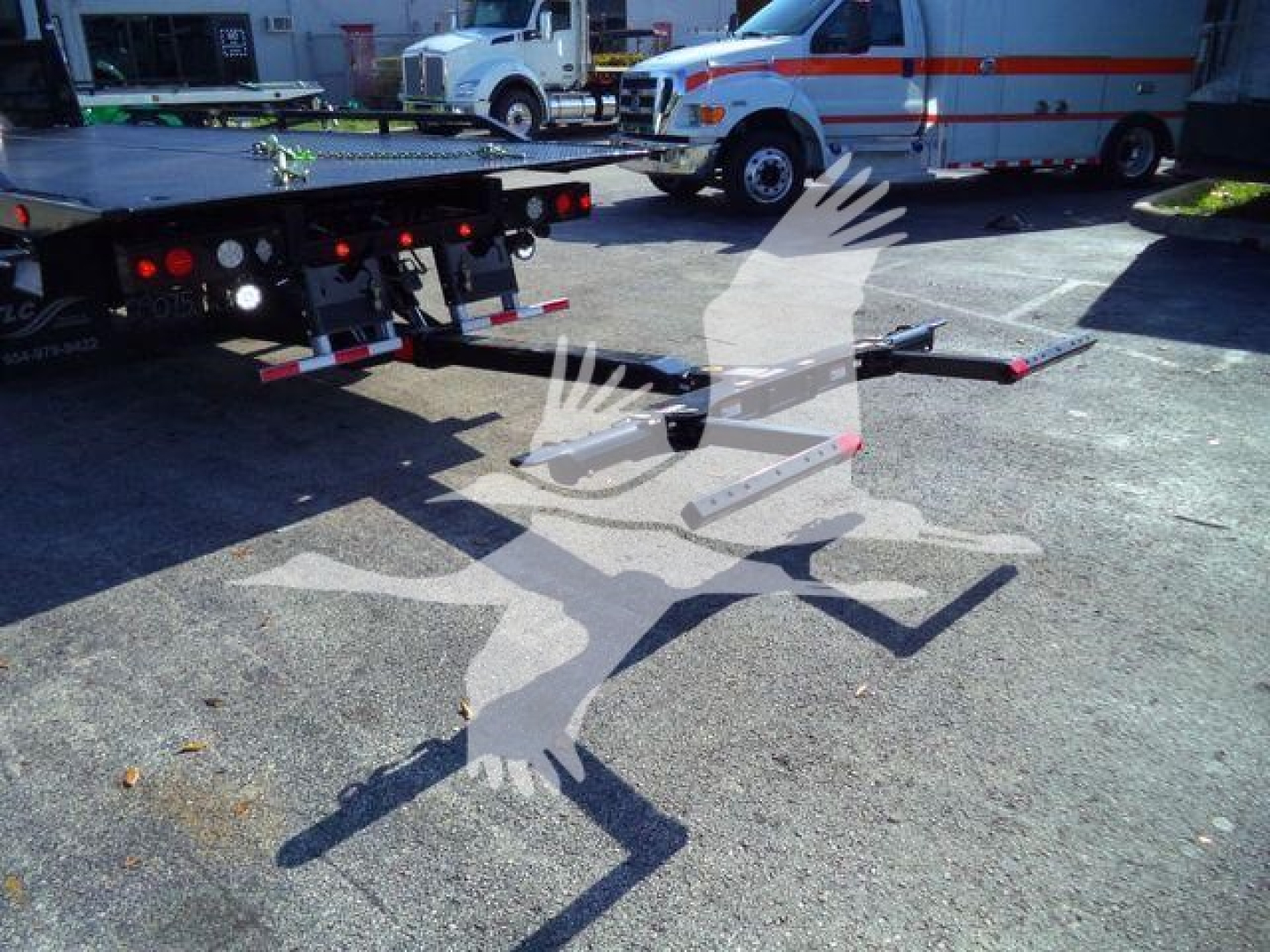 Peterbilt 536 rollback truck with trailer and loading ramps extended in parking lot, ambulance and truck in background.