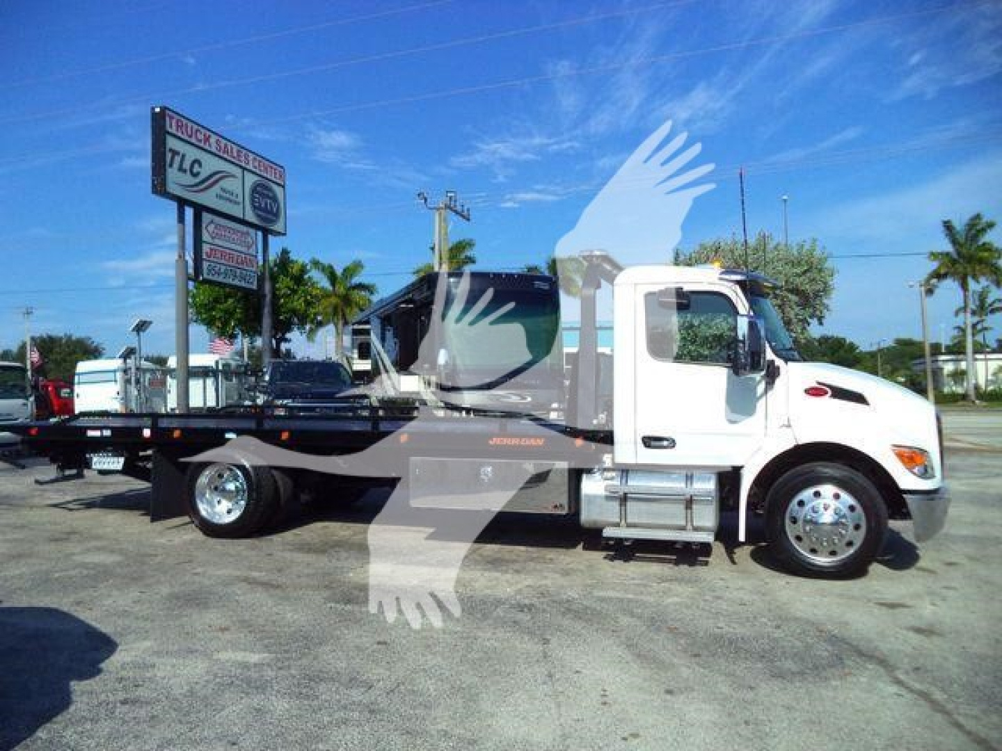 Peterbilt 536 rollback tow truck side view with flatbed, white cab, black flatbed, stock number 1PETE536XLP22, dealership lot in background.