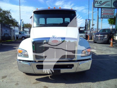 Peterbilt 536 rollback truck front view with prominent grille and bumper, white cab, dealership lot in background
