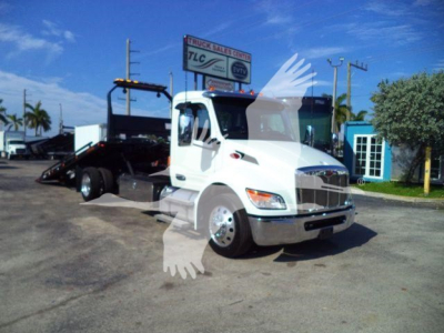 Peterbilt 536 rollback truck in white, front three-quarter view with flatbed and equipment mounting, dealership lot in background.