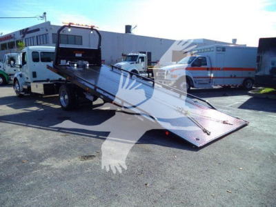 Peterbilt 536 rollback tow truck with lowered flatbed, in a dealership yard, with other emergency and service vehicles in background.