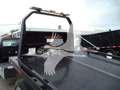 Flatbed tow truck bed with black diamond plate and rollover pickup rack. Visible branding JBERT? and orange warning stickers; light bar on cab frame.