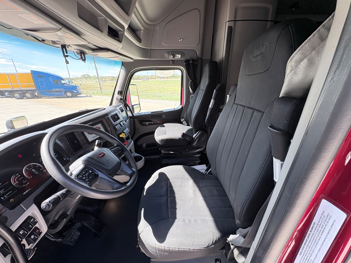 Truck cabin interior of a 2023 Peterbilt 579 with grey seats and steering wheel, driver and passenger seats visible.