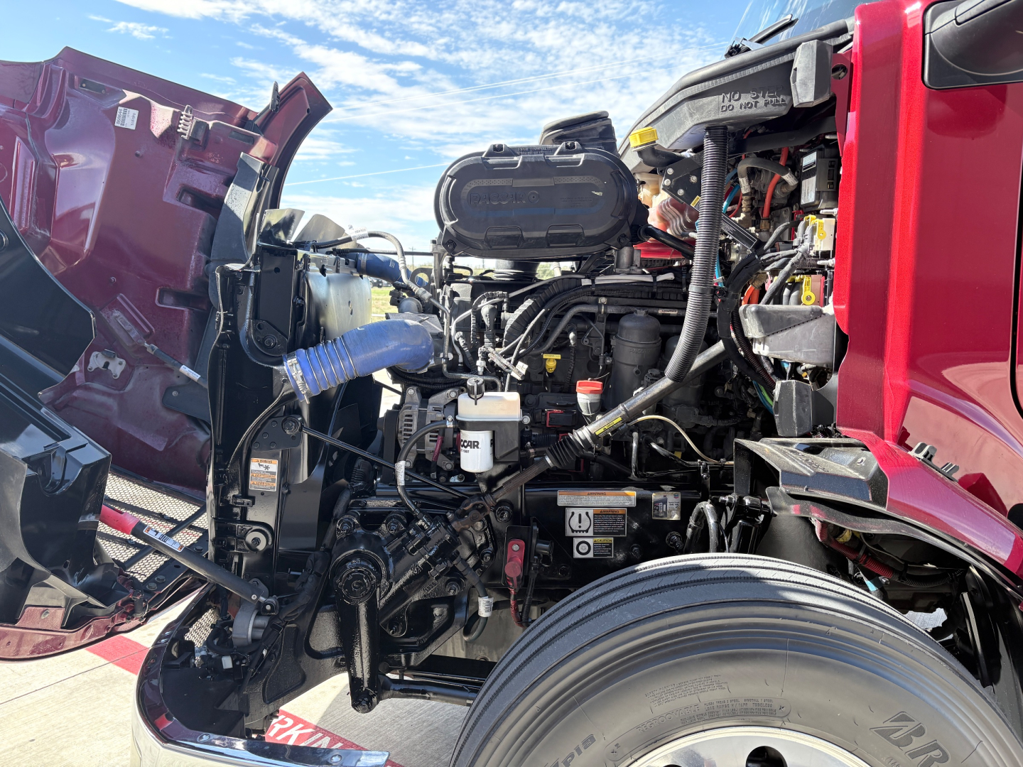 Peterbilt 579 engine bay showing main engine, hoses, and intake components with red cab and open hood.