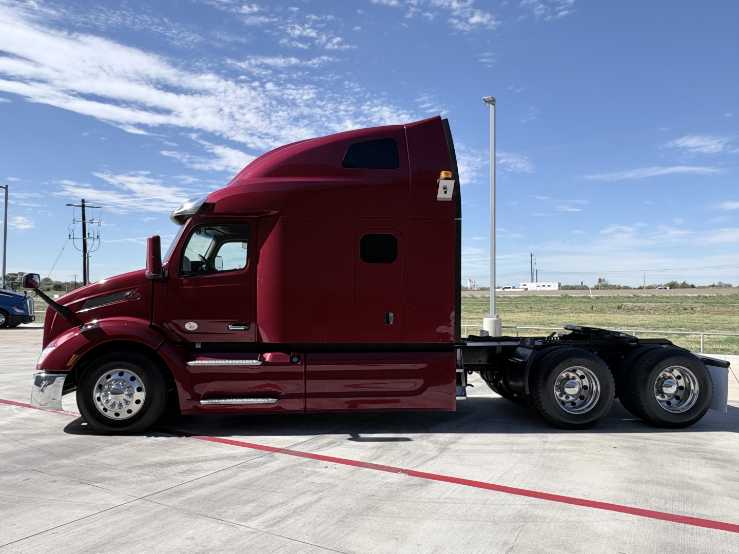 Peterbilt 579 tractor in red, side view profile with sleeper cab, three rear axles, chrome wheels, highway environment, no visible cargo.