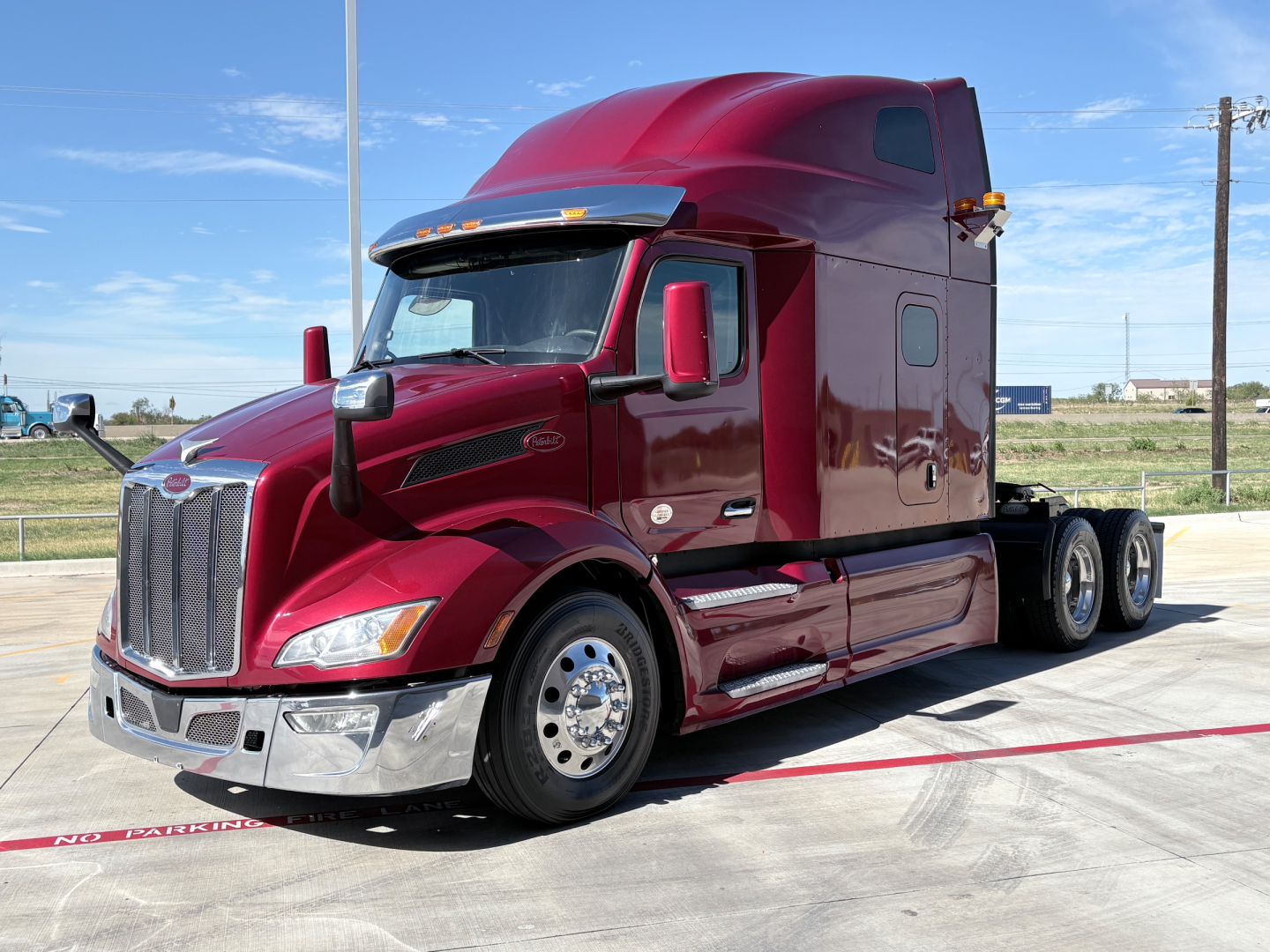 Peterbilt 579 tractor-trailer in maroon, front-left angle showing cab, sleeper, chrome grille, and dual rear axles.