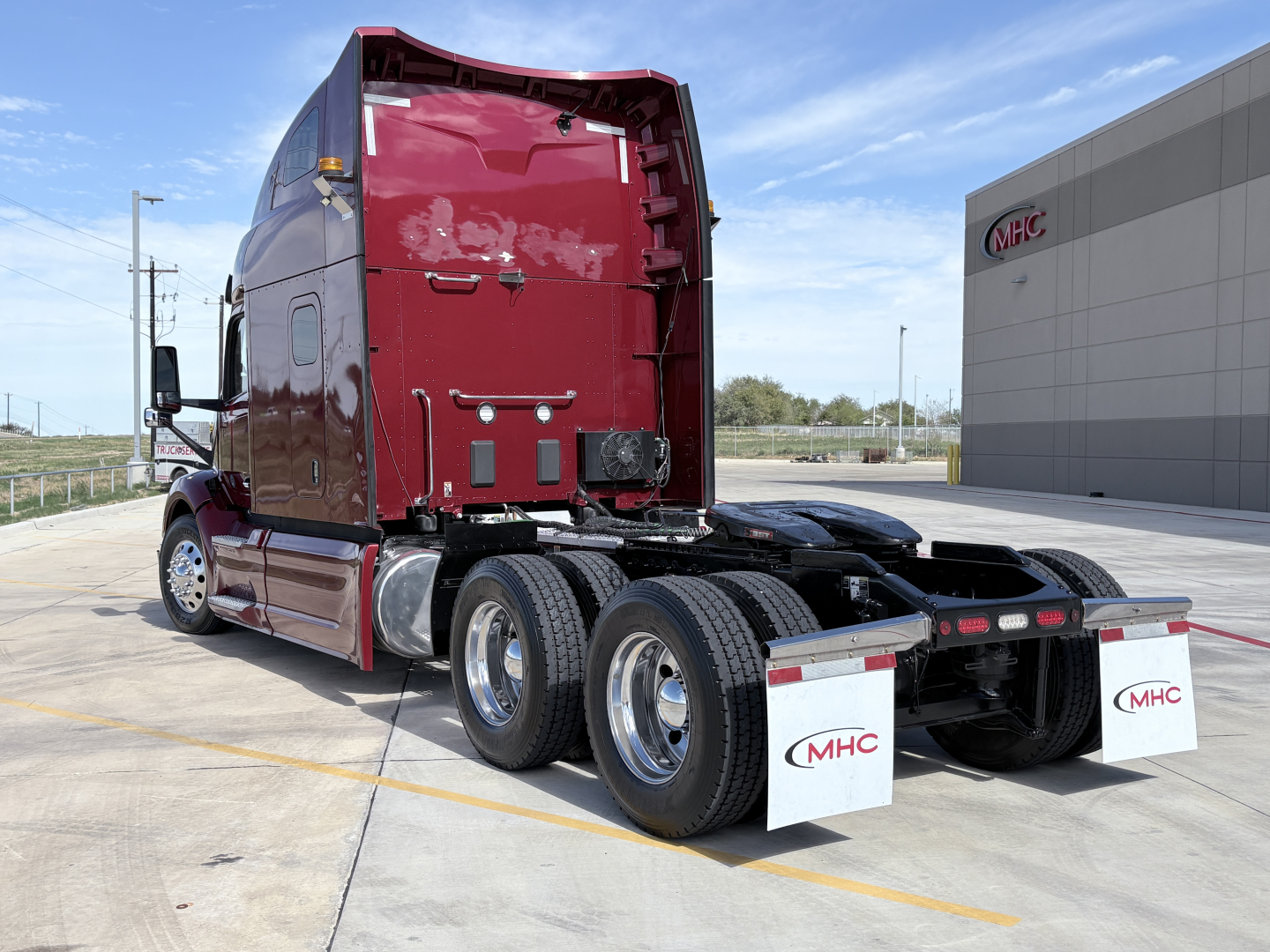 Peterbilt 579 truck rear view showing sleeper cab, dual rear axles, chassis, and mud flaps with MHC logo.